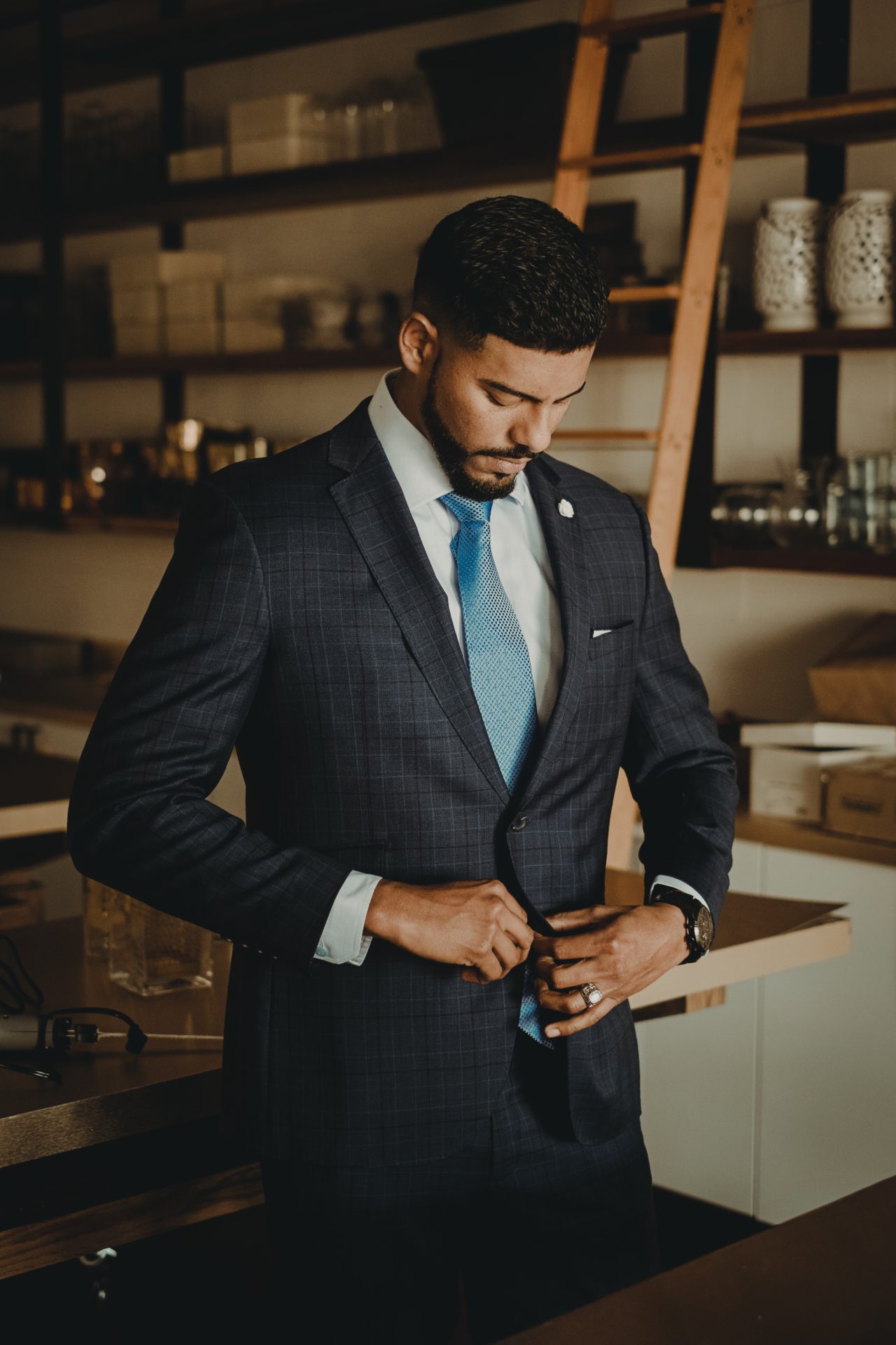 Man with beard standing up buttoning up suit with blue tie