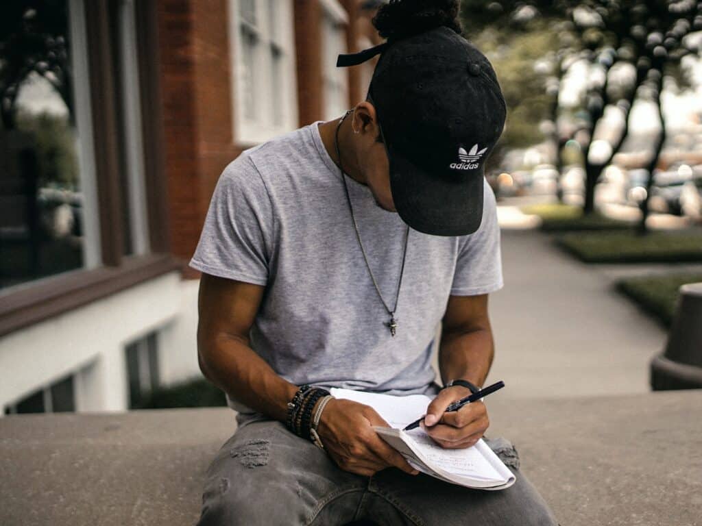 young man wearing a black cap writing on a notebook