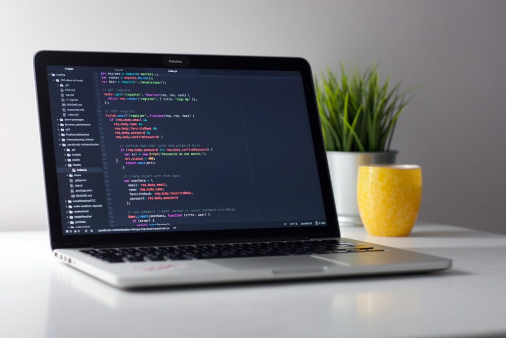 laptop with lines of code on a white desk with yellow mug