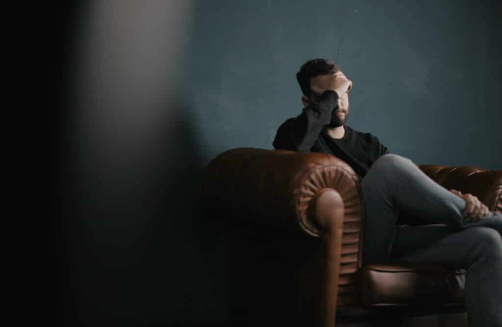 Sad looking man on brown sofa with hand on head