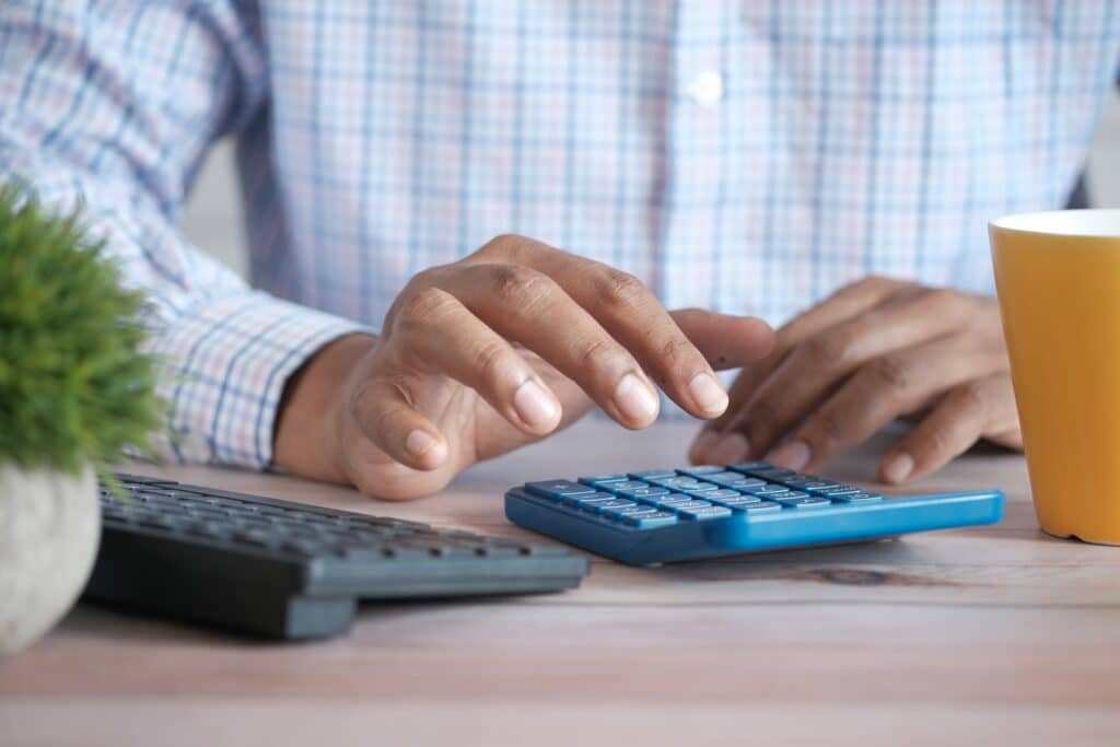 man wearing white/blue checkered shirt pressing a blue calculator